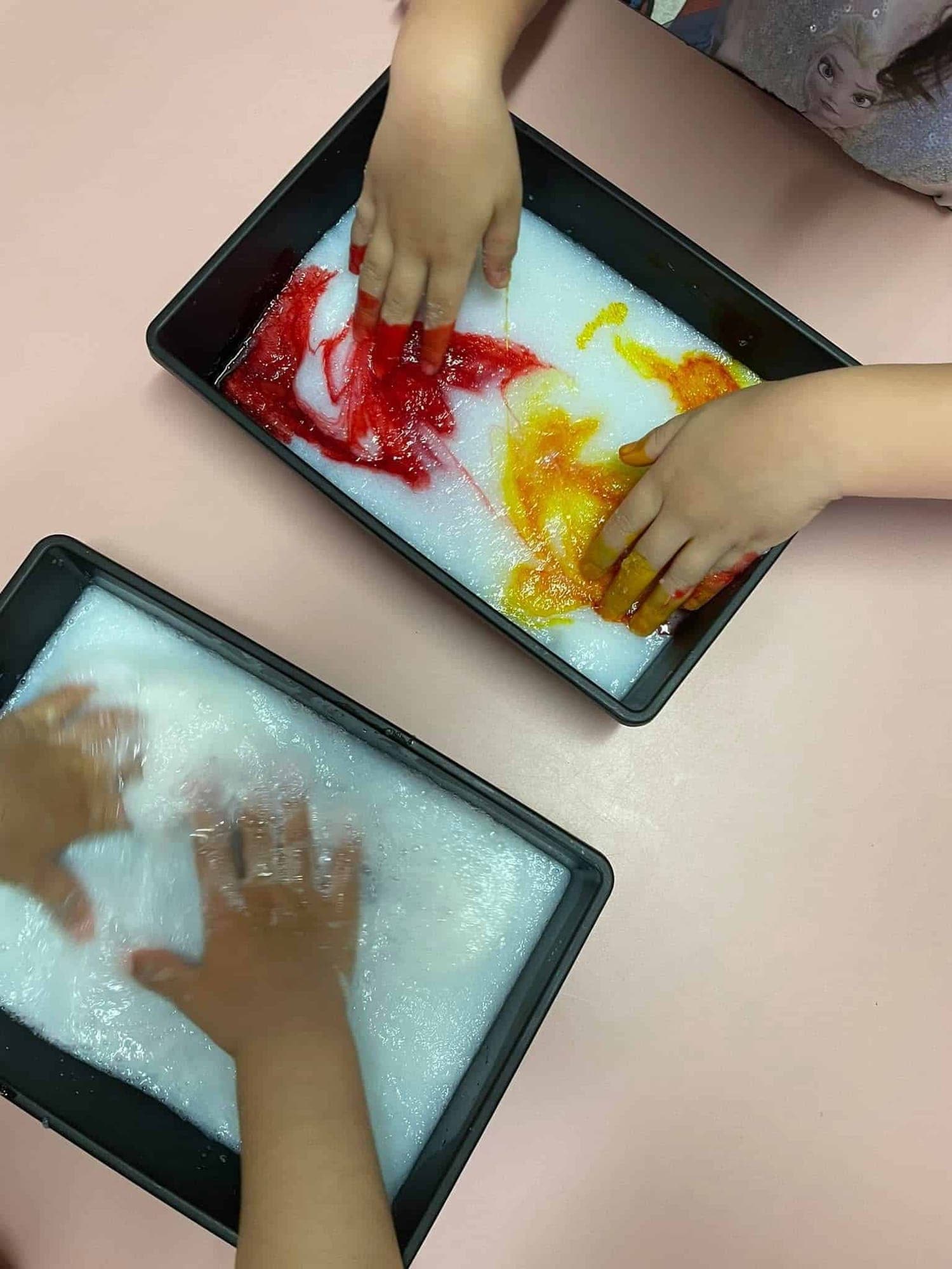 Small hands exploring trays of coloured sensory materials